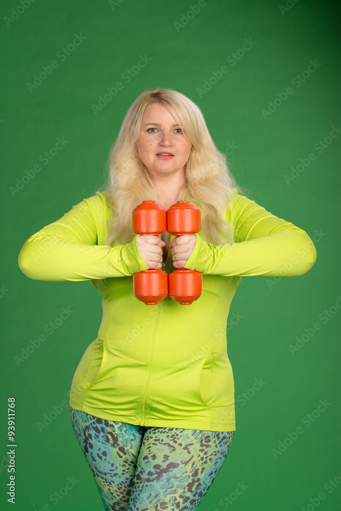 Plus size woman pumping up muscules with dumbbells on green back Plus size woman pumping up muscules with dumbbells on green back