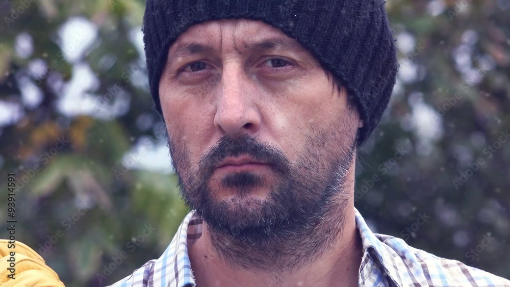 Serious confident lumberjack in snow, adult bearded man holding a big axe and looking at camera in outdoors surrounding, close up of face, treetop in background. Serious confident lumberjack in snow, adult bearded man holding a big axe and looking at camera in outdoors surrounding, close up of face, treetop in background.