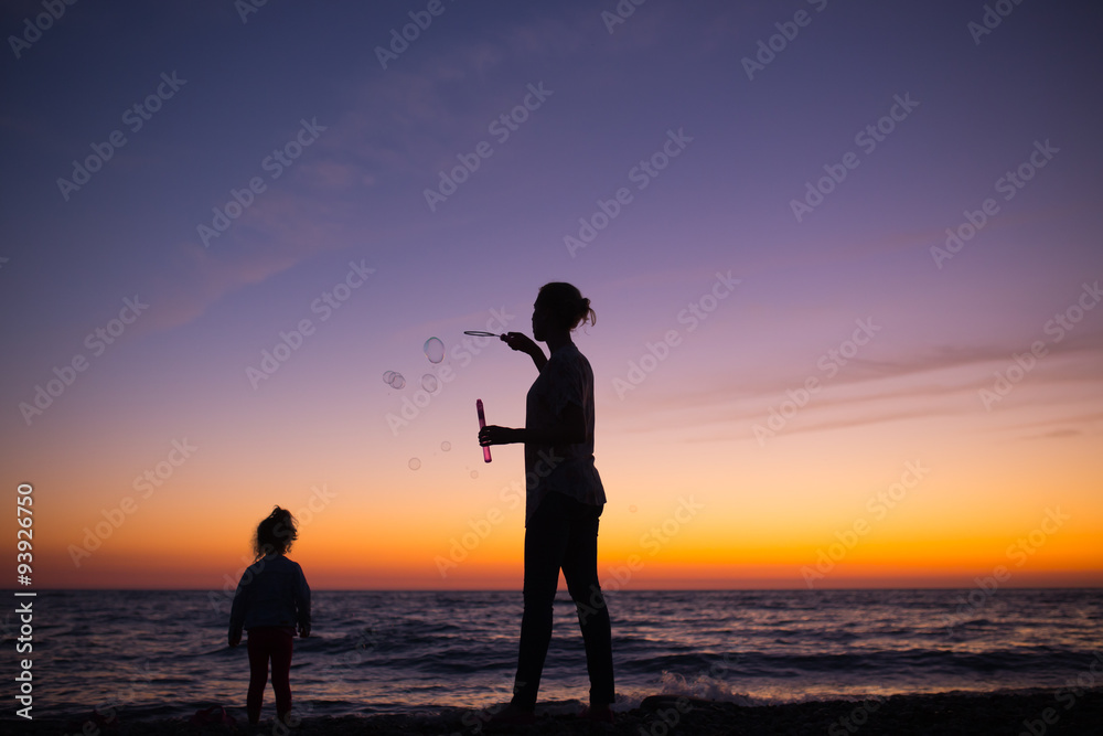 Fototapeta premium Silhouette of Mother and daughter playing with soap bubbles on t