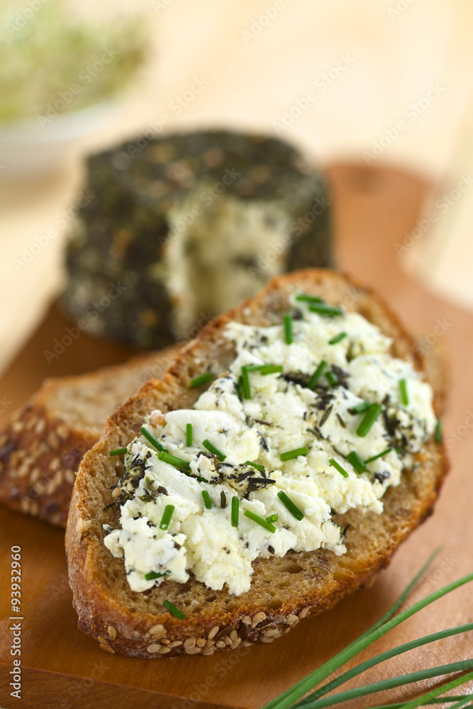 Slice of wholegrain bread spread with goat cheese with herbs with chives on top (Selective Focus, Focus one third into the cheese) Slice of wholegrain bread spread with goat cheese with herbs with chives on top (Selective Focus, Focus one third into the cheese)