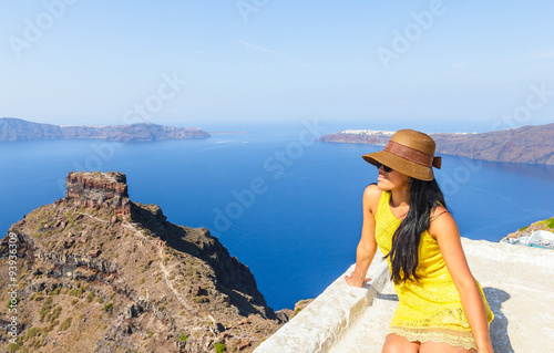 Attractive woman wearing hat and yellow dress enjoying the view of volcanic island in the early morning on Santorini  Mediterranean sea  Greece  
