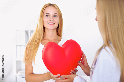 Woman doctor  in  hospital, a large red heart  in patient hand  at the background