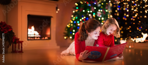 Mother and daughter reading at fire place on Christmas eve © famveldman