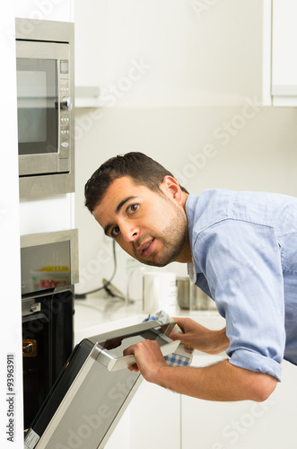 Hispanic male wearing blue shirt in modern kitchen leaning