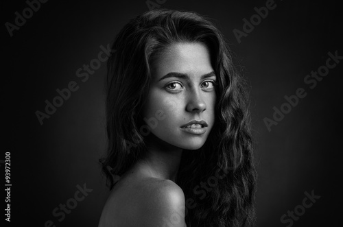 Dramatic portrait of a girl theme: Black and white portrait of a young beautiful girl on a dark background in the studio