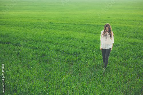 Outdoor full body portrait of sad lonely girl in green field. Young woman walking in meadow with copy space.