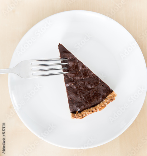 Piece of chocolate tart or pie on a white ceramic dish with stainless steel fork (top view)