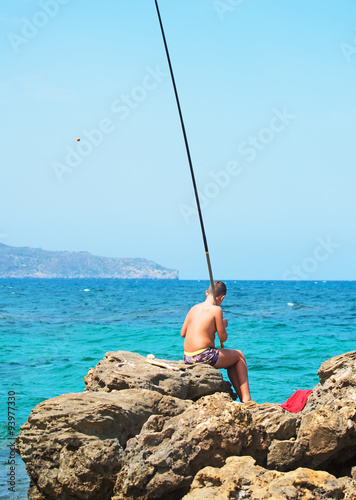 Boy fishing on rocks by the sea.