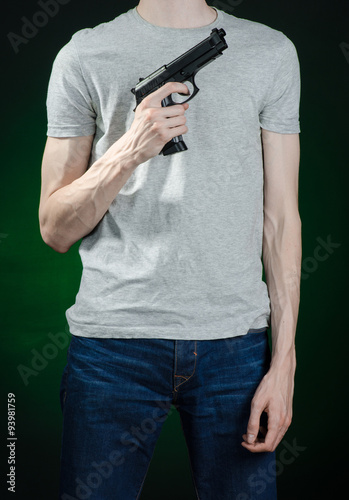 Firearms and murderer topic: man in a gray t-shirt holding a gun on a dark green background isolated in studio