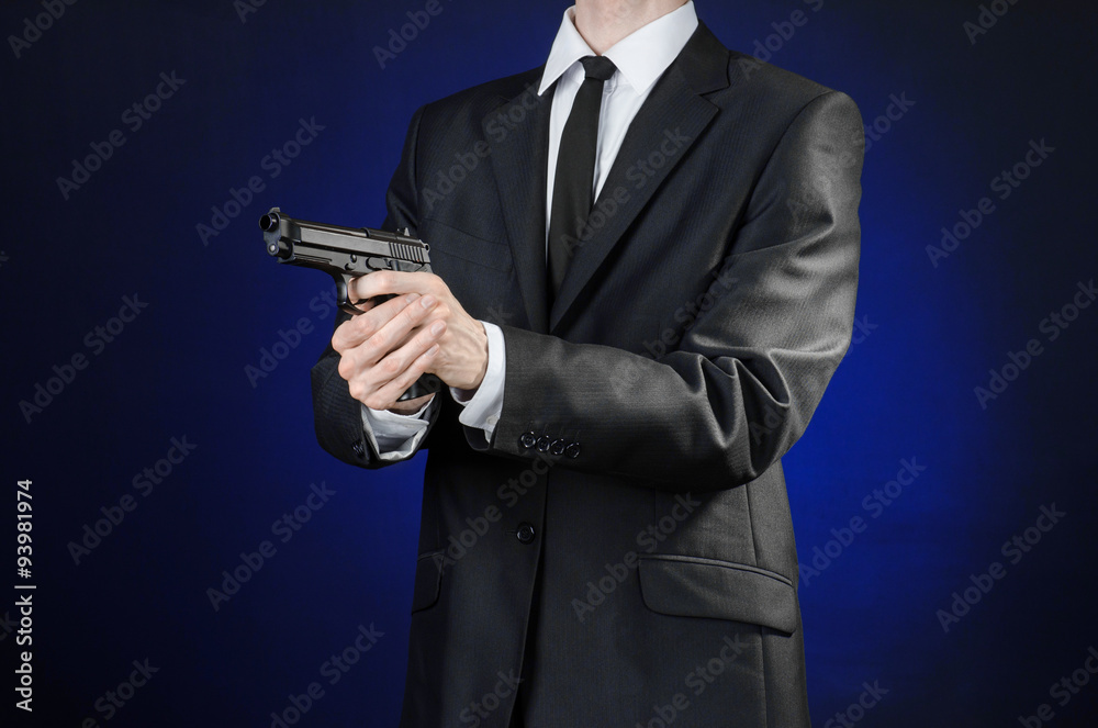 Firearms and security topic: a man in a black suit holding a gun on a dark blue background in studio isolated Firearms and security topic: a man in a black suit holding a gun on a dark blue background in studio isolated