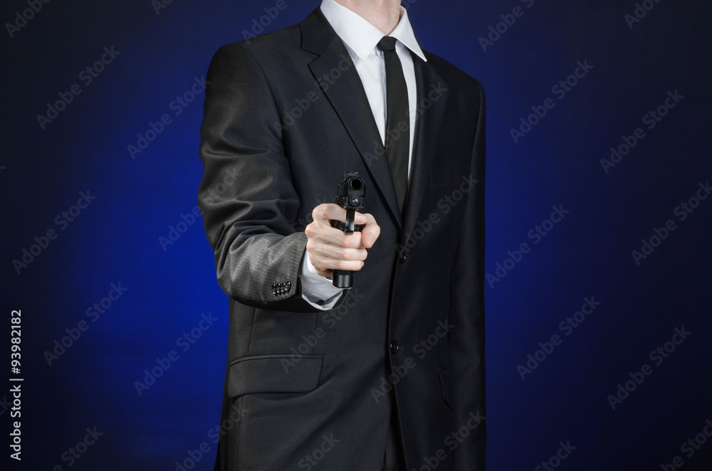 Firearms and security topic: a man in a black suit holding a gun on a dark blue background in studio isolated
