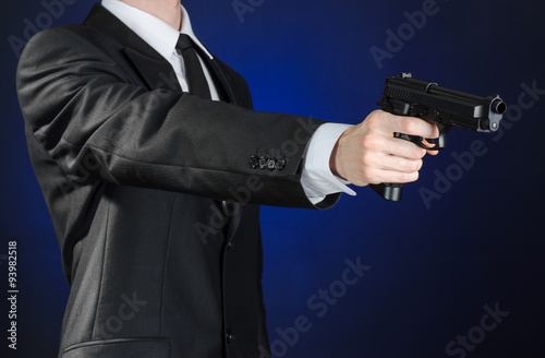 Firearms and security topic  a man in a black suit holding a gun on a dark blue background in studio isolated