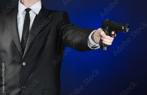 Firearms and security topic: a man in a black suit holding a gun on a dark blue background in studio isolated