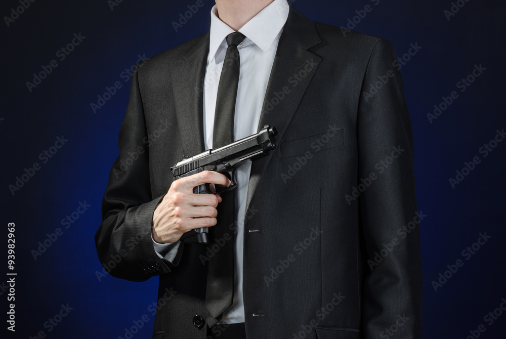 Firearms and security topic: a man in a black suit holding a gun on a dark blue background in studio isolated Firearms and security topic: a man in a black suit holding a gun on a dark blue background in studio isolated