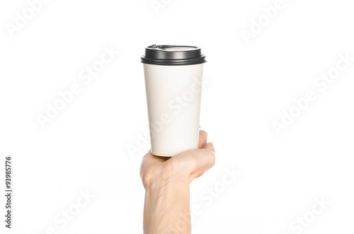 Breakfast and coffee theme: man's hand holding white empty paper coffee cup with a brown plastic cap isolated on a white background in the studio, advertising of coffee first-person view