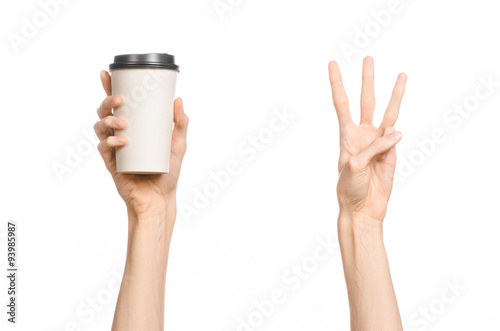Breakfast and coffee theme: man's hand holding white empty paper coffee cup with a brown plastic cap isolated on a white background in the studio, advertising coffee