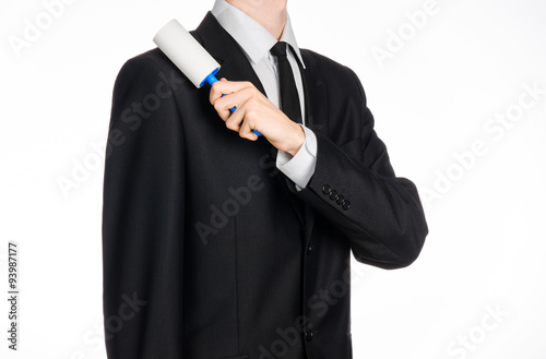 Dry cleaning and business theme: a man in a black suit holding a blue sticky brush for cleaning clothes and furniture from dust isolated on white background in studio.