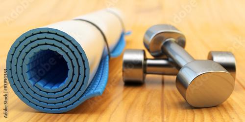 Fitness workout and slimming exercises concept  weight loss gym equipment  blue yoga mat and black metallic dumbbells on wooden floor of training class