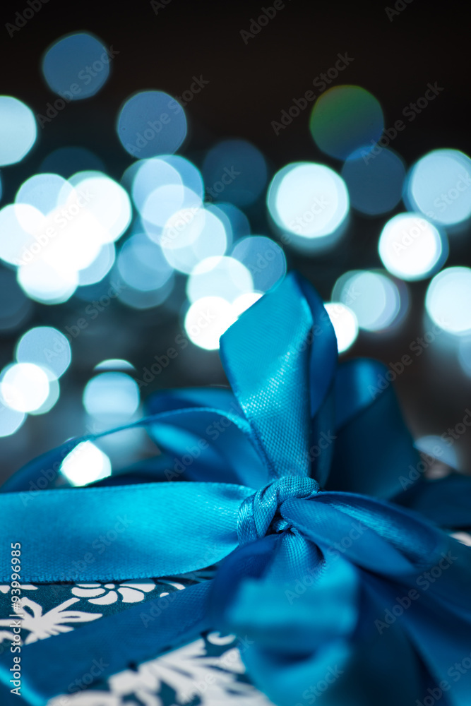 Christmas gift box with blue bow and lights on wooden surface Christmas gift box with blue bow and lights on wooden surface