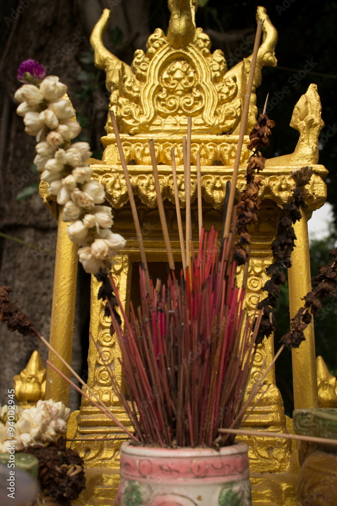 Extreme close up detail of a gold spirit house in Southeast Asia, with incense and flowers at center (vertical)