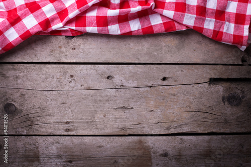 Red checkered kitchen towel on vintage wooden background.