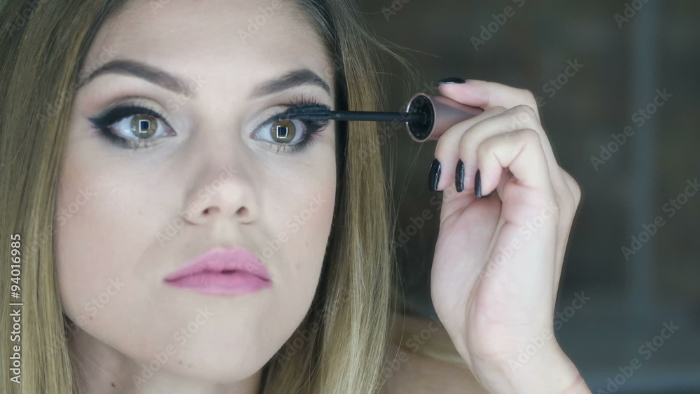 Pretty woman applying mascara to her eyelashes in front of bathroom mirror Pretty woman applying mascara to her eyelashes in front of bathroom mirror