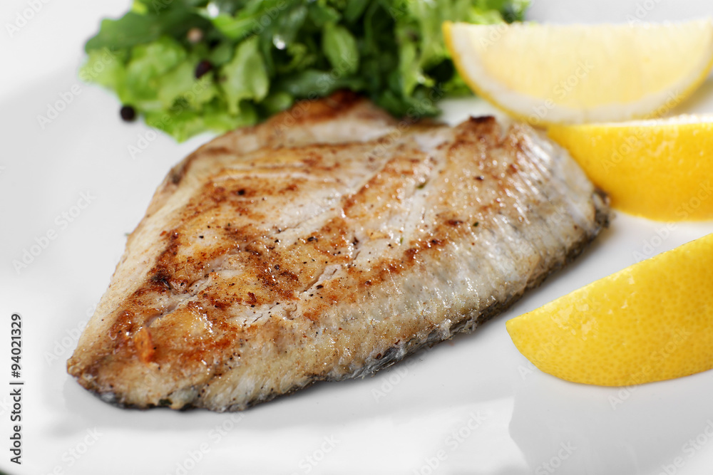 Dish of fish fillet with greens and lemon on plate close up Dish of fish fillet with greens and lemon on plate close up