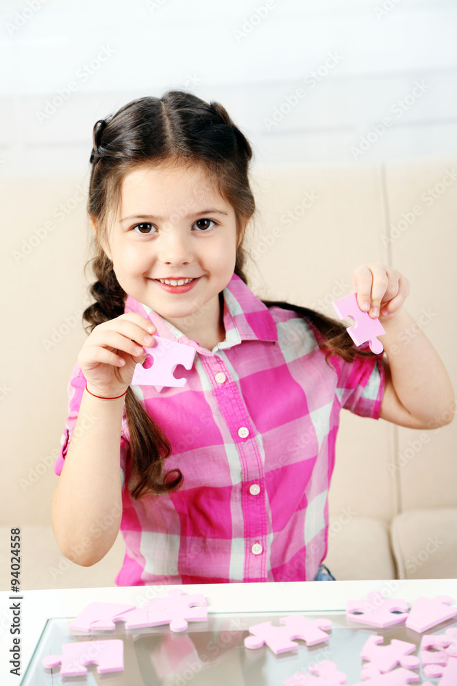 Cute little girl playing with puzzles on home interior background Cute little girl playing with puzzles on home interior background