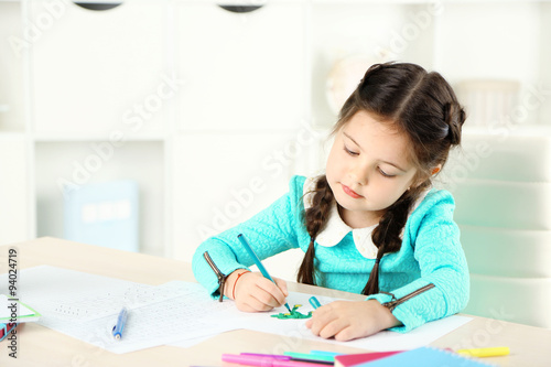 Cute little girl doing her homework, close-up, on home interior background