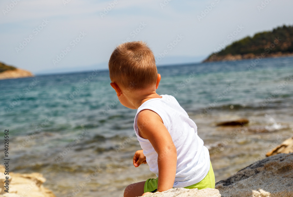 Rear view of little boy sitting on the rock beach, Rear view of little boy sitting on the rock beach,