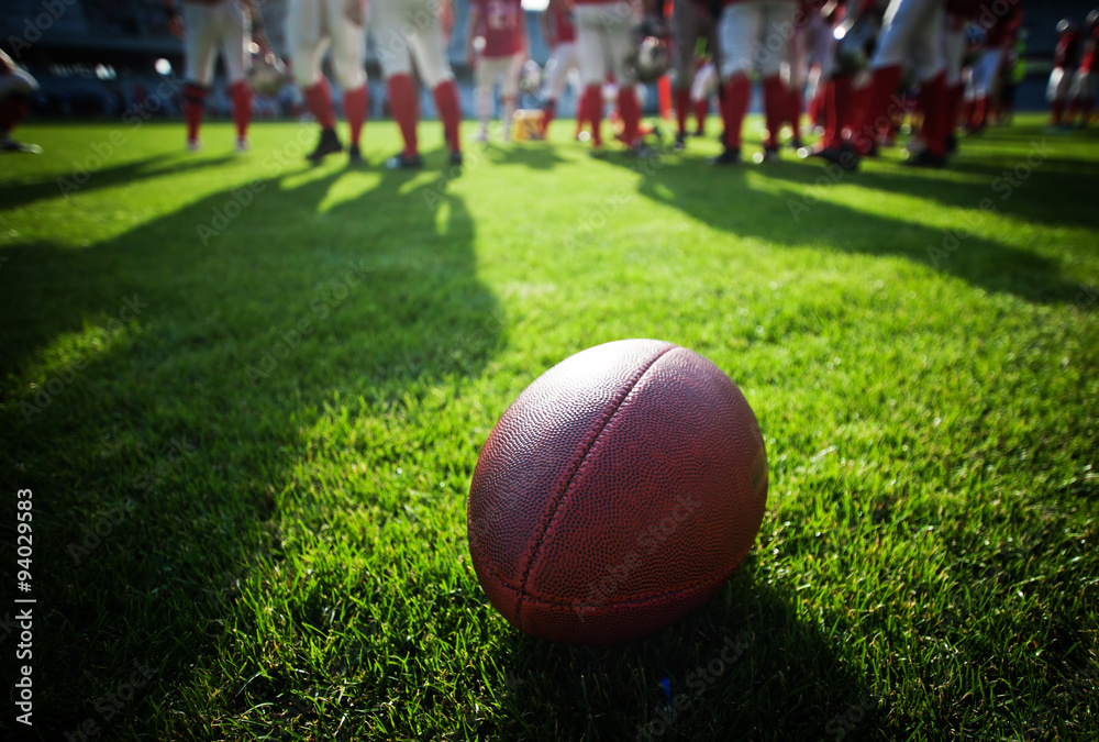 Close up of an american football on the field, players in the ba Close up of an american football on the field, players in the ba
