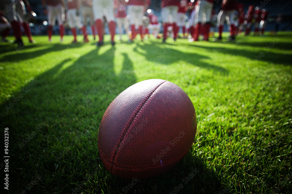 Close up of an american football on the field, players in the ba Close up of an american football on the field, players in the ba
