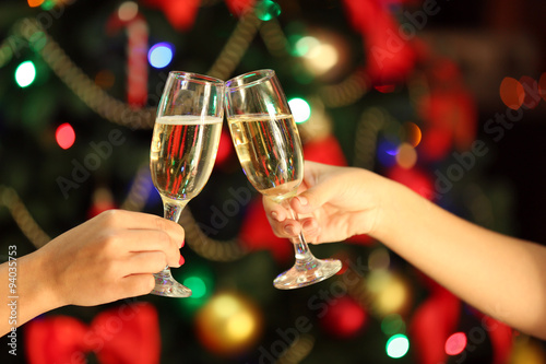 Clinking glasses of champagne in hands on bright lights background