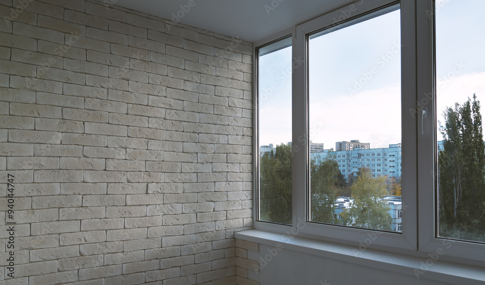 Fototapeta premium Balcony window beside white brick wall provides a bright interior view of urban apartment buildings, ideal for real estate design, home renovation, and architectural marketing