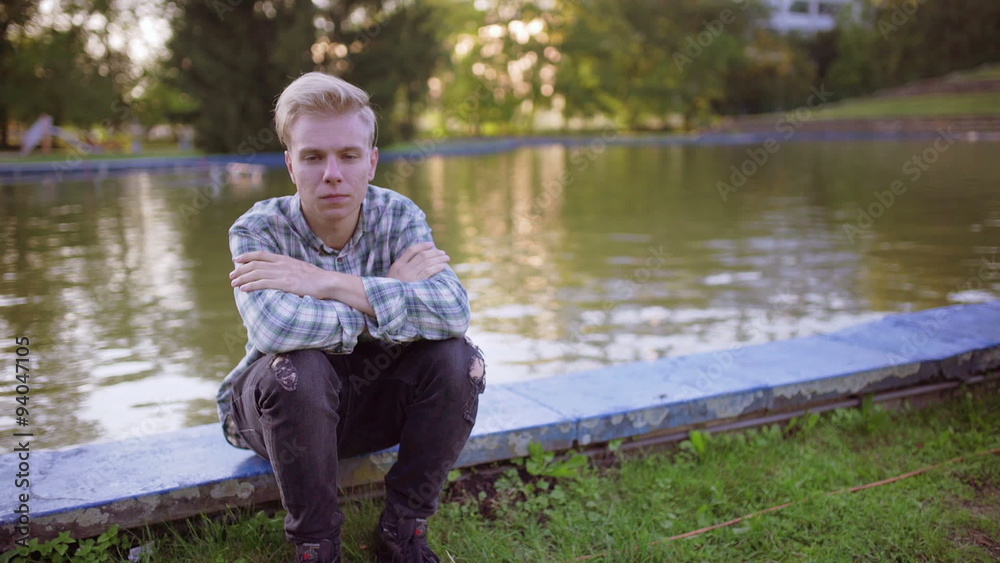 Unhappy boy sitting next to the pond and looking to the camera
Unhappy boy sitting next to the pond and looking to the camera