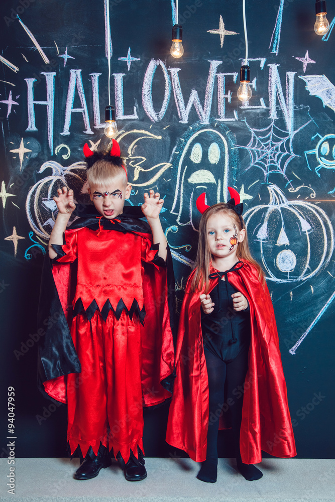Fototapeta premium Girl and boy, dressed up in Halloween costumes, show emotions of witches . Halloween party with group children.