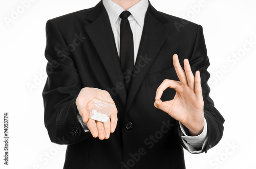 Addiction and business topic: hand in a black suit holds bag with white pills a drug on a white isolated background in studio