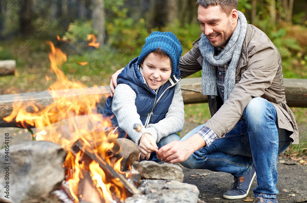 father and son roasting marshmallow over campfire - obrazy, fototapety, plakaty 