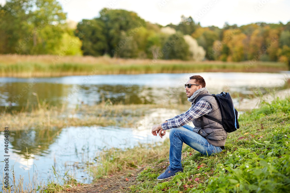 man with backpack resting on river bank man with backpack resting on river bank
