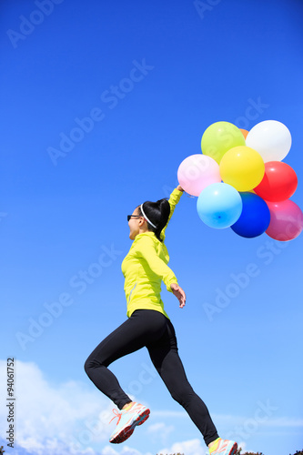 cheering young woman running on mountain peak with colorful bal
