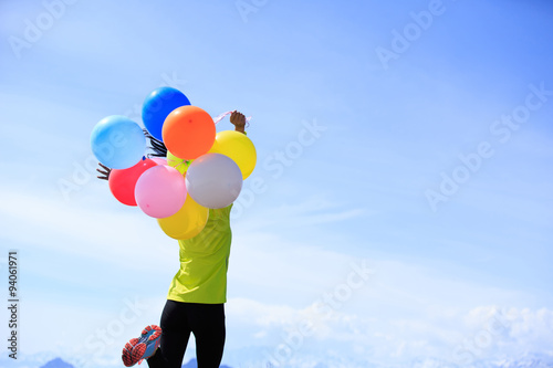 cheering young woman  running on mountain peak with colorful bal photo