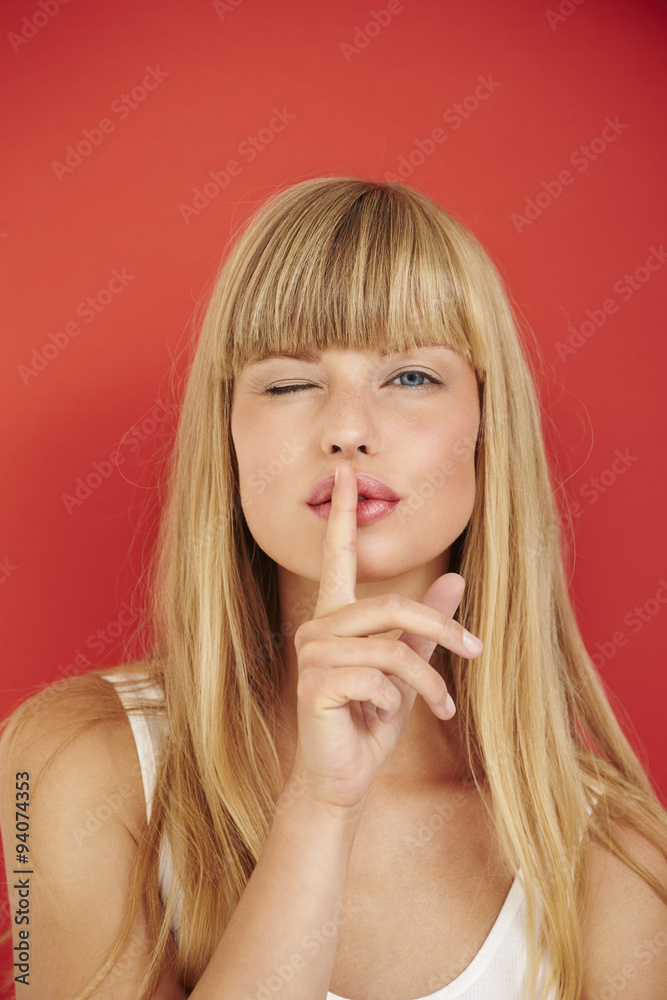 Naklejka premium Young blond woman with finger on lips against red