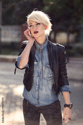 portrait of a young punk style blond woman outdoor, talking with her mobile phone