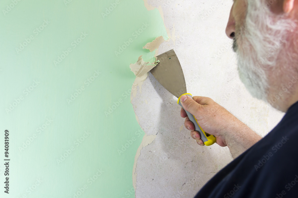 DIY man wallpaper stripping. Using a stripping tool to remove old