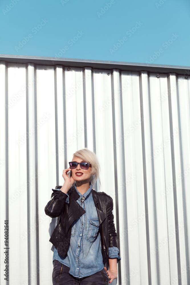 Fototapeta premium young punk style blond lady leaning on wall and using her mobile phone