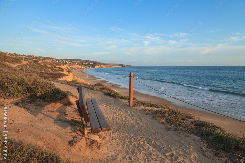 Obraz premium Bench along an outlook with a view at sunset of Crystal Cove Beach, Newport Beach and Laguna Beach line in Southern California