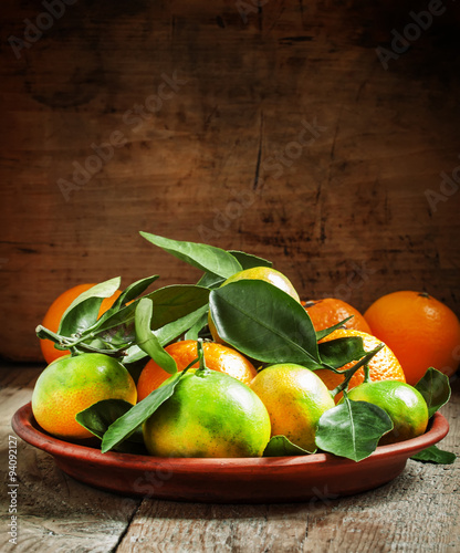 Orange and green ripe tangerines with leaves on a clay plate on