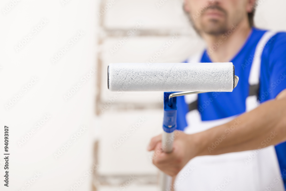 Close up shot of painter man aiming at you with paint roller.