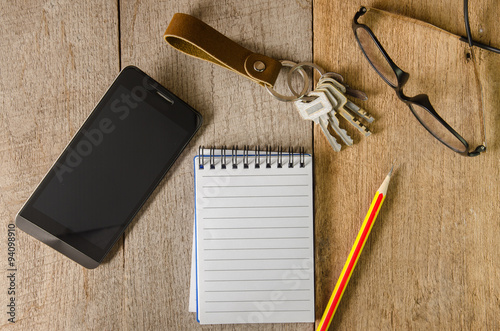 Blank notepad, key chain, eye glasses and mobile phone on wooden