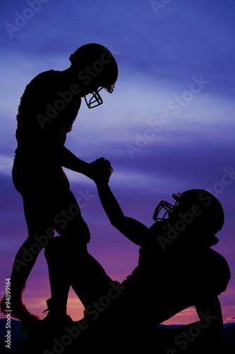 silhouette of one football player helping another up